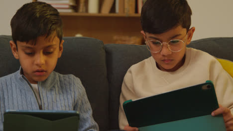 Two-Young-Boys-Sitting-On-Sofa-At-Home-Playing-Games-Or-Streaming-Onto-Digital-Tablets-3